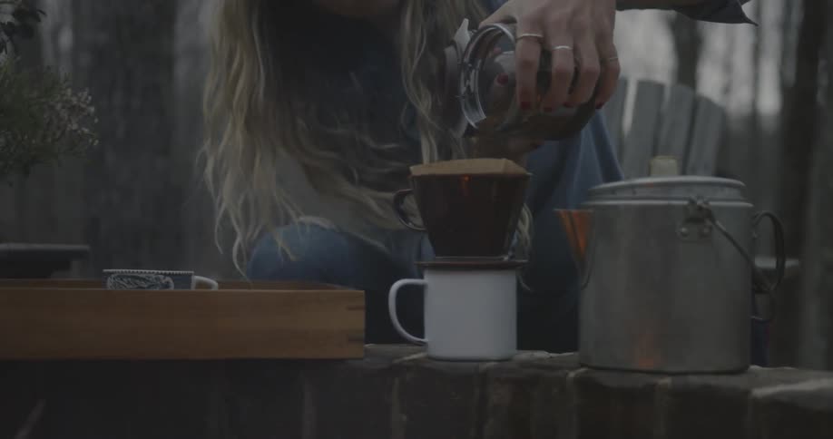 Long-haired woman  pouring something through a filter into a cup