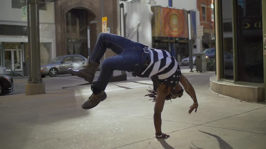 An african american male is performing a flip on a sidewalk in an urban area