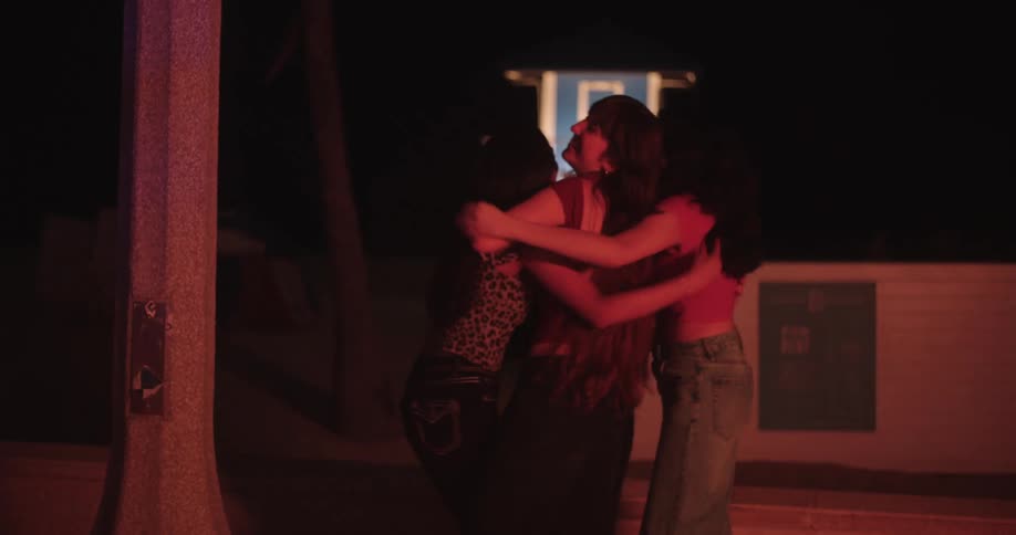 Three young female friends happily hugging each other in an outdoor location at night