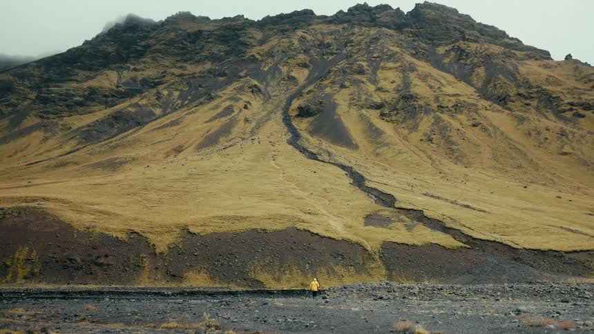 Person in a yellow jacket walking towards a towering mountain