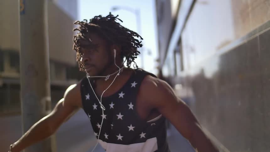 A black man is standing on a sidewalk in a city dancing