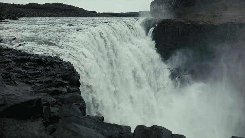 A powerful waterfall cascades over rocky cliffs creating white wash and mist that rises above the waterfall