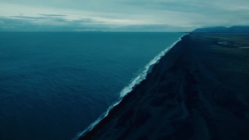 Aerial landscape of a black land area surrounded by the sea on a cloudy day