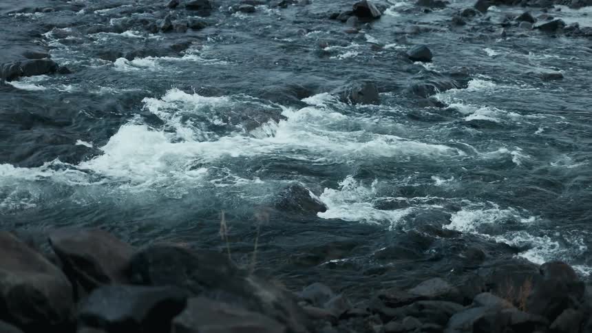 Dark rocks are scattered in and around turbulent water as the river flows eastward