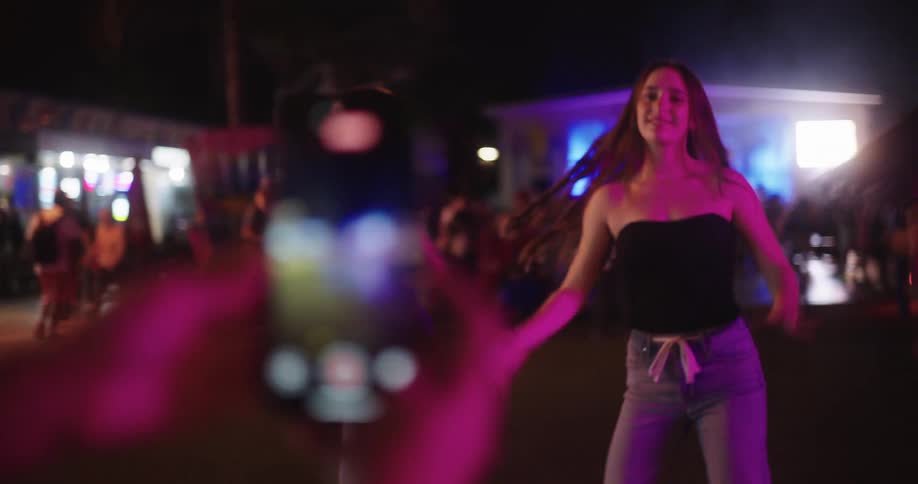 Three young women dancing together and being filmed by an iphone camera
