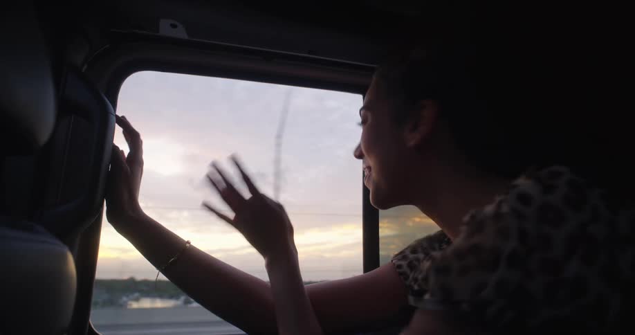 Woman enjoying the breeze in the window of a car and moving with the force of the wind and dancing happily