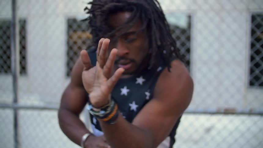 Man dances in front of a chain link fence