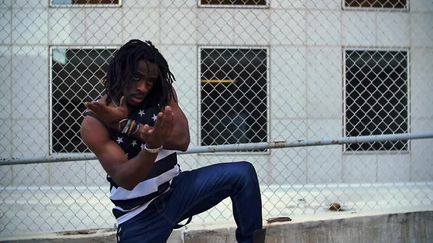 An african american male is performing a dance in an urban area during the day