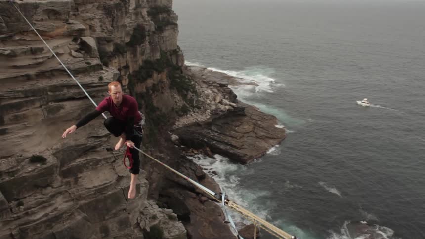 Man walks on a tightrope between  cliffs
