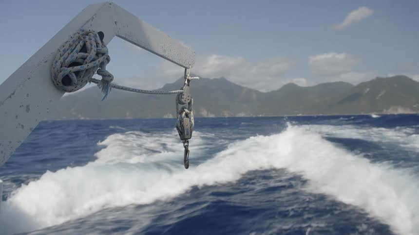 A boat rides on the water with a hook hanging