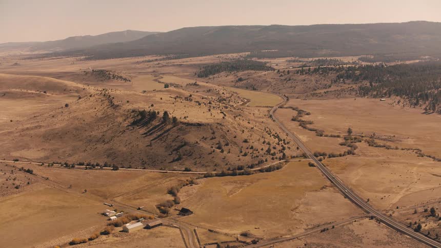 Aerial view of a dry landscape with areas of sparse vegetation a winding road and hills in the background