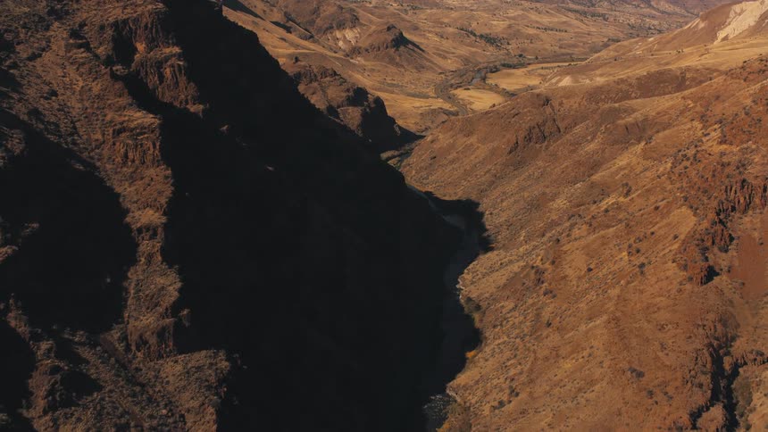 A rugged arid landscape with steep rocky hills and a deep shadowed canyon running through the center