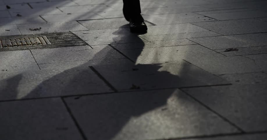 Person in black leather shoes walking on a city street