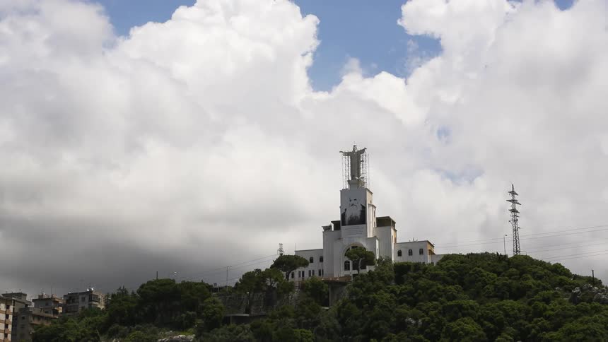 Church with a statue on top under construction on a hill with clouds above