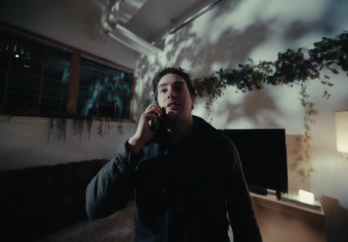 A man in a dark jacket talks on his smartphone in the living room at night in front of the television