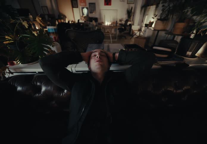 Man leaning back in a black armchair with his hands on his head