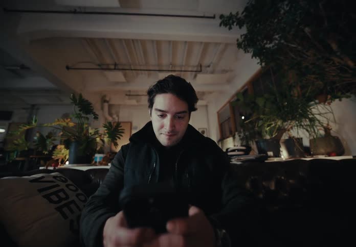 Young man sitting in a black armchair typing on a smartphone