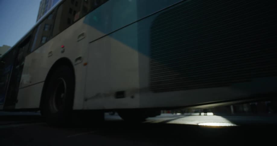 A bus is driving on a city street with cars in the background and sunlight shining between tall buildings