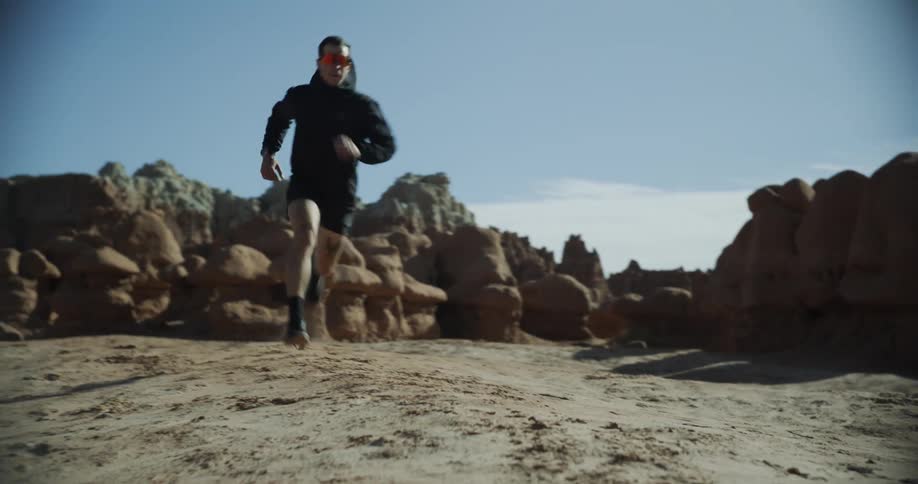 A person is running in a desert landscape with rugged hills in the background under a partly cloudy sky