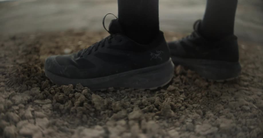 A person is standing on a gravel surface wearing darkcolored running shoes
