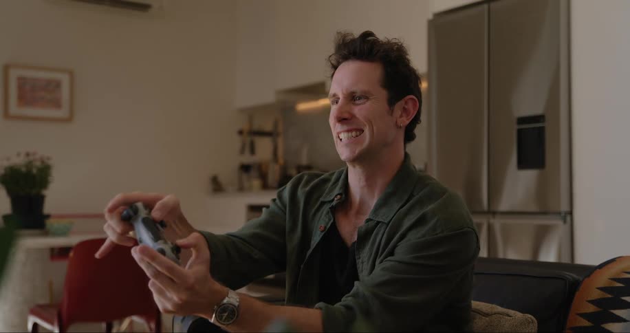 A man is sitting on a couch in a modern living room playing a video game