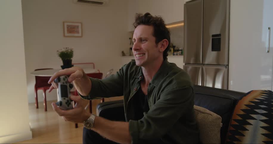 A man is sitting on a couch in a modern living room playing a video game