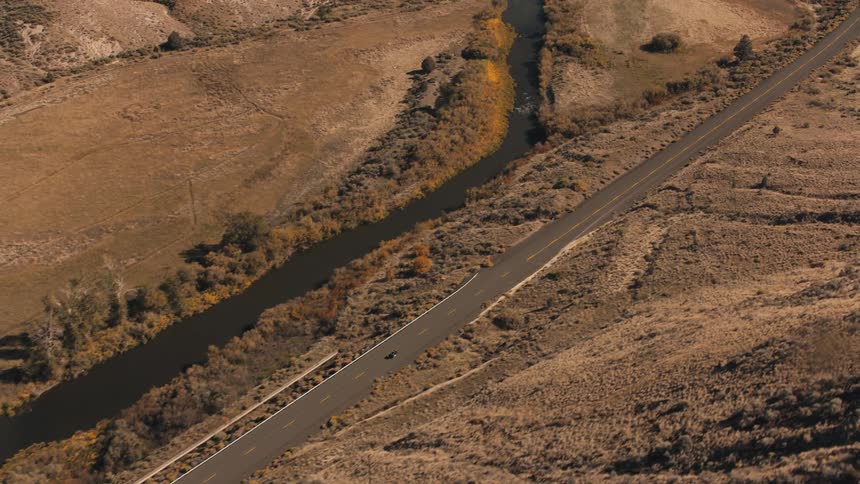 Paved road runs parallel to a river in an arid landscape seen from above