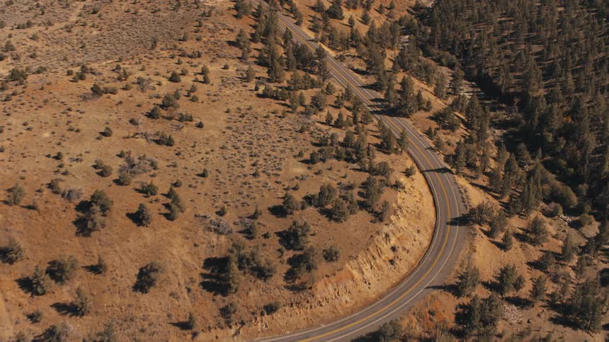 A winding road cuts through a vast arid landscape of rolling hills and sparse vegetation