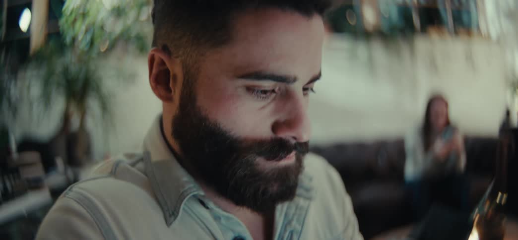 The face of a bearded man who is using his cell phone and typing quickly on the screen