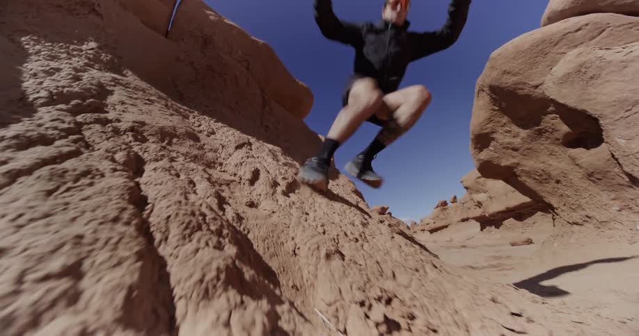 A person jumping off a rocky formation in a desertlike landscape with clear blue skies