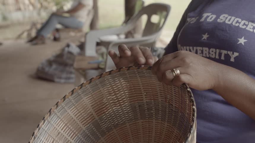 A woman is sitting outside weaving a basket