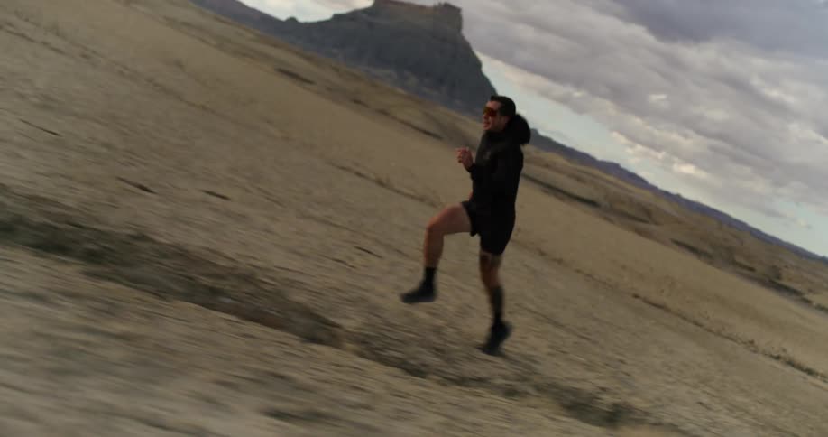 A person is running in a desert landscape with rugged hills in the background under a partly cloudy sky