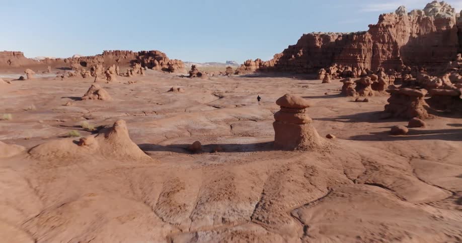 An adult is running through a desert with large rock formations on a mostly sunny day