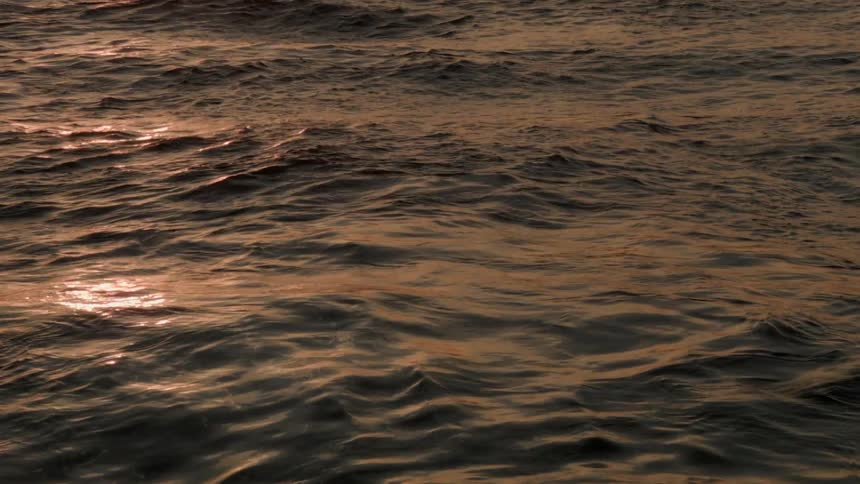 A body of water making waves with the sun setting