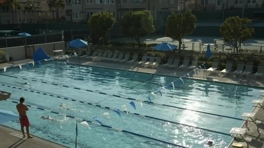 People swimming laps as a man stands at the pool edge coaching them
