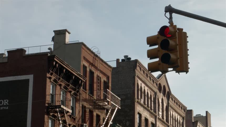 A traffic light hangs from a pole with buildings in the background