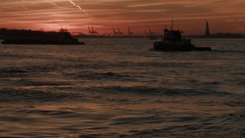 Boats float with the statue of liberty in the background at sunset