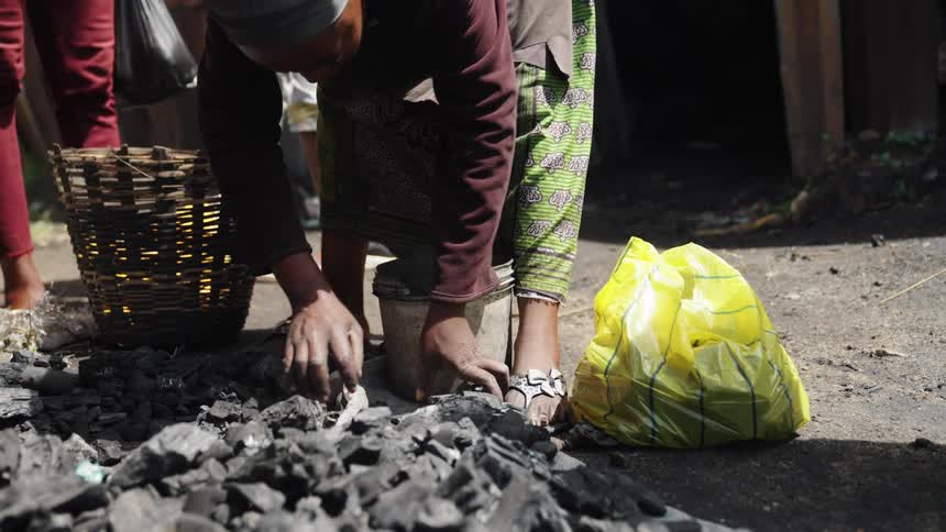 Woman fills a bucket with rocks lying on the ground