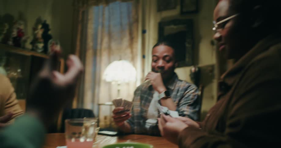 Friends play cards at a dining table at night