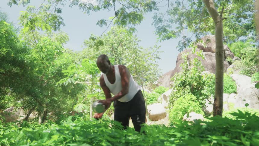 Man waters plants in a garden near a rock mound on a summer day