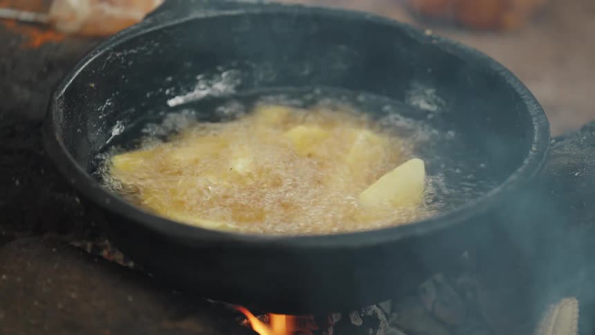 Close up of a frying pan frying potatoes on a wood stove