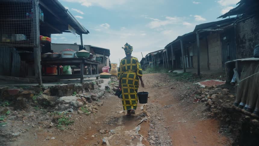 Woman in a third world country walking through a village carrying buckets of water