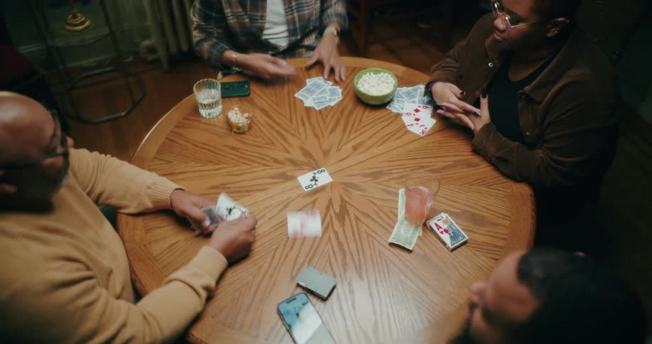Four people sitting at a round wooden table playing cards