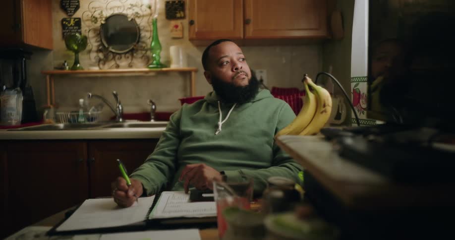 Bearded man sitting at a table writing in a notebook and getting thoughtful