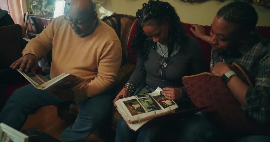 Three people sitting on a red sofa armchair looking at photo albums