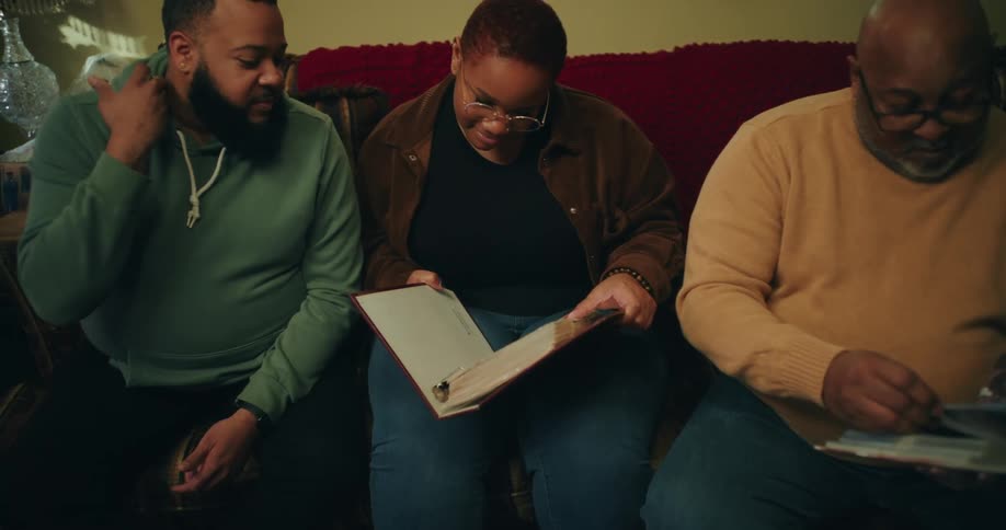 A family sits closely together on a couch looking at photo albums or books in a warmly lit room