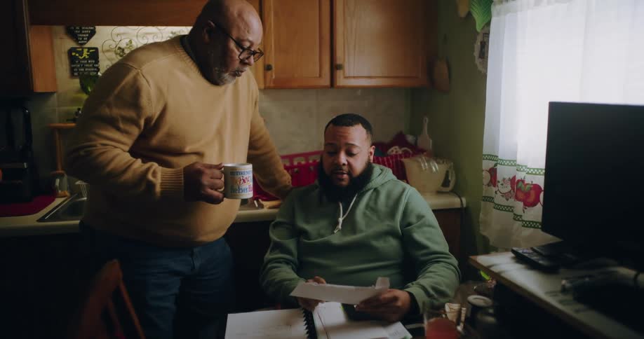 A father and son discuss paperwork in the kitchen