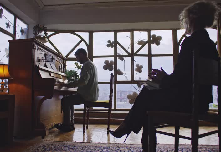 A footage of a person playing a piano and a lady watching