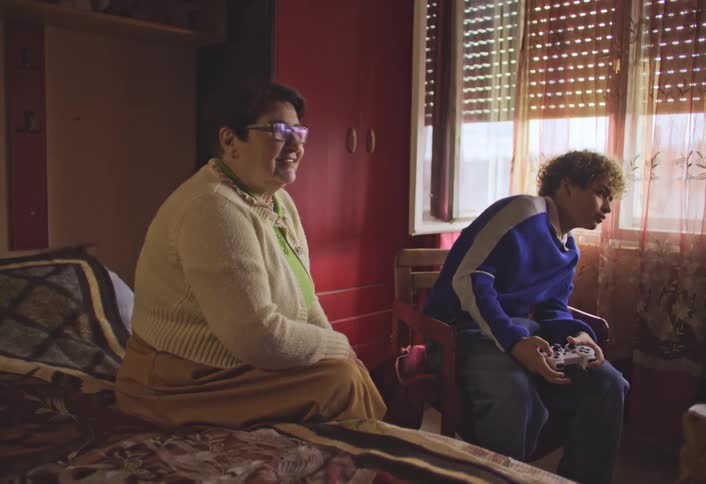A mother watches her son playing videogames in his bedroom