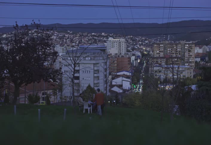 Man sitting at an outdoor table on a hill with his friends and overlooking an urban city